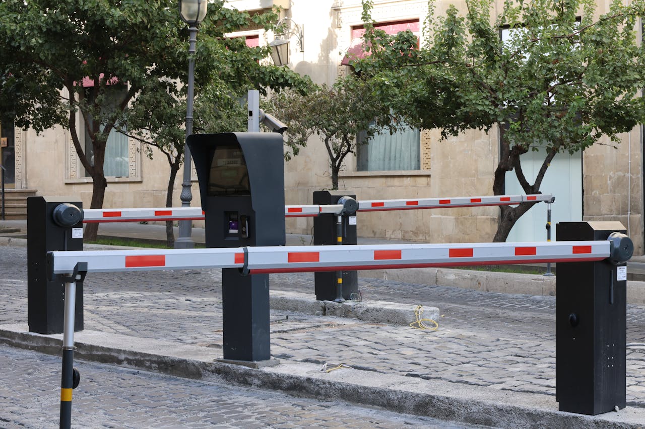 Modern parking barrier gate system on cobblestone street with greenery.