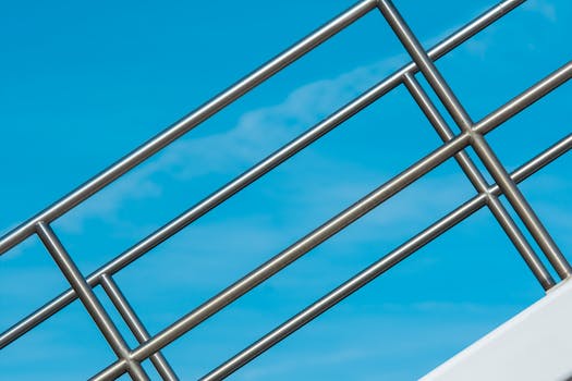 Close-up of a sleek steel railing set against a vibrant blue sky, showcasing modern architecture.